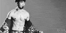 a black and white photo of a shirtless man singing into a microphone on a stage .