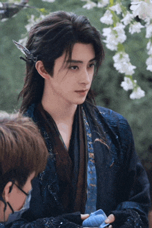 a man with long hair is standing in front of a flowering tree