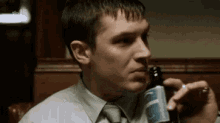 a man in a tie is drinking a beer from a bottle .