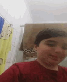 a young boy taking a selfie in a bathroom with towels hanging on the wall behind him