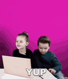a boy and a girl are sitting at a table with a laptop computer .