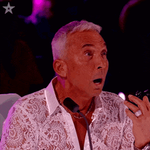 a man in a lace shirt is speaking into a microphone with a star in the background