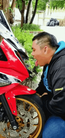 a man with his tongue out looks at a red motorcycle with gold rims