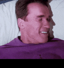a man in a purple shirt is smiling while laying in a bed