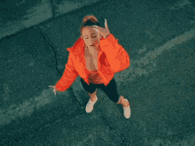 a woman in an orange jacket stands on a street