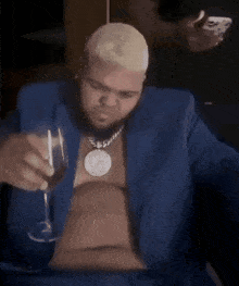 a man in a blue suit is sitting at a table holding a glass of wine .