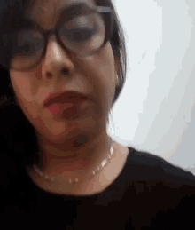 a woman wearing glasses and a necklace is making a funny face