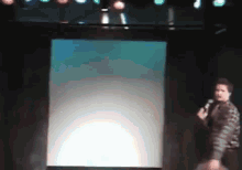 a man stands on a stage holding a microphone in front of a screen