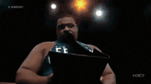 a man is reading a book in a dark room with a wwe nxt logo on the bottom