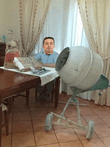 a man sits at a table next to a concrete mixer and a bag of cement
