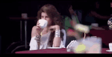 a woman is drinking from a cup while sitting at a table .