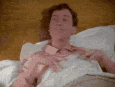 a man in a pink shirt is laying in a bed with white sheets