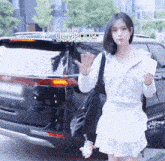 a woman in a white dress is standing in front of a black kia