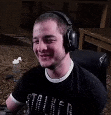 a man wearing headphones and a black shirt is smiling while sitting in a chair .