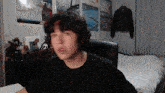 a man in a black shirt is sitting in front of a bed with posters on the wall
