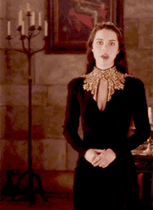 a woman in a black dress and gold collar is standing in front of a candelabra