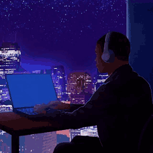 a man wearing headphones sits at a desk using a laptop