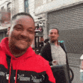a man wearing a red and black puma sweatshirt smiles