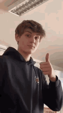a young man wearing a black hoodie is giving a thumbs up .