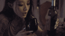 a woman drinks from a glass next to a bottle of wine