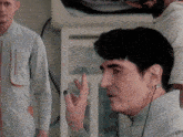 a man wearing ear buds talks into a microphone while another man looks on