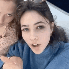 a woman in a blue sweater is taking a selfie with another woman in a pink dress .