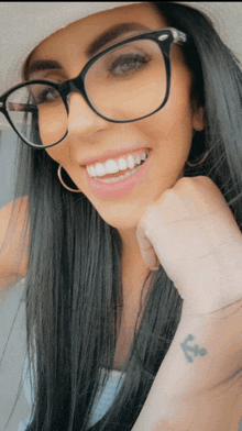 a woman wearing glasses and a hat has a small tattoo of an anchor on her wrist