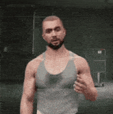 a man with a beard wearing a tank top is standing in a dark room