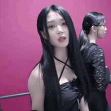 a woman with long black hair is standing in front of a pink background