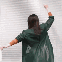 a woman in a green coat is dancing with her arms outstretched .