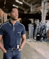 a man in a blue polo shirt is standing with his hands in his pockets in a warehouse .