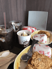 a table topped with plates of food and drinks including a cup that says ' jollibee ' on it