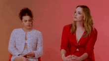 two women are sitting next to each other in front of a red background .