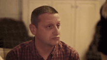 a man in a plaid shirt is making a funny face and looking at the camera .