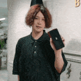 a man in a green polo shirt is holding a black phone with a x on it