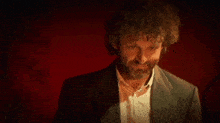 a man with curly hair and a beard is standing in a dark room .