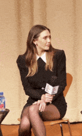 a woman in a black dress sits in a chair holding a microphone that says ' cbs news ' on it