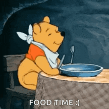 winnie the pooh is sitting at a table with a plate of food and a spoon in his mouth .