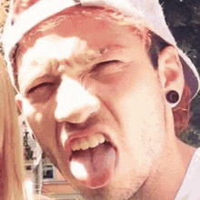 a man wearing a hat and ear plugs is sticking out his tongue .
