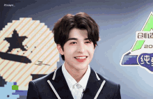 a young man in a suit smiles in front of a sign that says it says