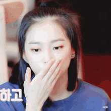 a woman is covering her mouth with her hand while wearing a blue sweater .