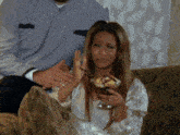 a woman is sitting on a couch with a bowl of food in her hand