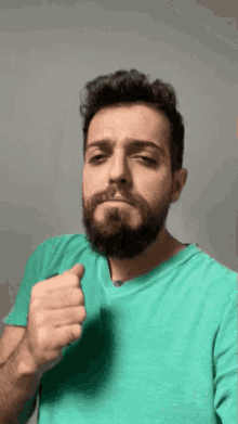 a man with a beard is wearing a green shirt and giving a thumbs up sign