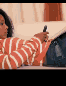 a woman in a striped shirt is laying on a couch looking at her cell phone
