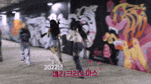 a group of girls are dancing in front of a wall with graffiti on it that says 2022