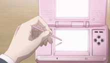 a hand is holding a pink pen over a pink nintendo ds game console