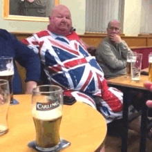 a man is sitting at a table with a carling glass of beer