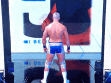 a shirtless wrestler is standing in front of a large screen that says i be