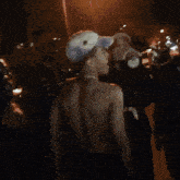 a shirtless man wearing a hat and a necklace stands in a crowd of people