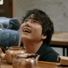 a man is sitting at a table with a teapot in front of him and looking up